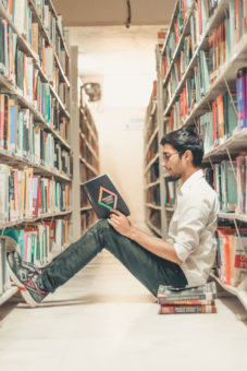 student in library reading book on floor